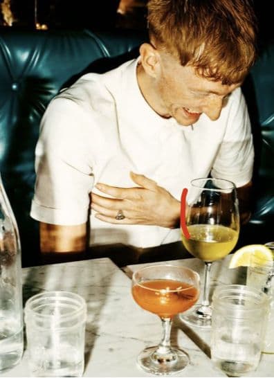 A man laughing in a leather booth, cocktails on the table